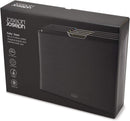 The image shows a Joseph Joseph Folio 4-Piece Cutting Board Set. It consists of a sleek, dark-colored (likely black or dark gray) storage case that holds four individual cutting boards. The tops of the cutting boards are visible, showing different colored tabs, which are typically used for hygienic separation of food types (e.g., raw meat, vegetables, cooked food, fish). The Joseph Joseph logo is visible on the lower front of the case.