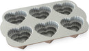 Toffee-colored Nordic Ware cakelet pan with six tiered heart-shaped cavities, displayed on a white background.
