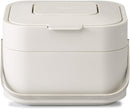 Joseph Joseph stone-colored compost bin with stainless-steel handle and flip-top lid shown on a white background.