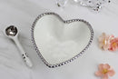 A white heart-shaped porcelain bowl with a silver beaded rim, accompanied by a matching white spoon. Dimensions of the bowl (5.5" x 5.5" x 2.5") and spoon (5" long) are indicated.