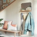 A sleek white wall-mounted organizer mirror with rounded corners, featuring a light wood shelf beneath it. Below the shelf, a white bar extends with several wooden peg hooks.