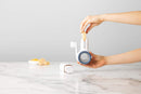 Chef'n spring-loaded rotary grater in white with blue accents, shown with a removable grating drum, designed for easy cheese grating.