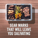 Grilling and serving set by Yukon Glory, featuring a large silver pan and three smaller black grill/sear trays with cooked food, plus a handle, all next to its product packaging.