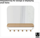 A sleek white wall-mounted organizer mirror with rounded corners, featuring a light wood shelf beneath it. Below the shelf, a white bar extends with several wooden peg hooks.