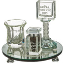 A beautifully designed clear crystal Havdalah set on a round mirror base with silver accents. The set includes a Kiddush cup, a square spice box, and a tall candle holder, all elegantly engraved with Hebrew text.