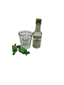 A mini bottle of Smirnoff Green Apple Vodka (50ml), a Fox Run 1.5 oz Measuring Shot Glass, and two sour green apple candies arranged on a clean white background.