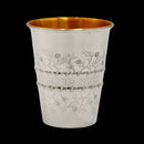  A close-up of a silver-plated Kiddush cup with engraved floral patterns and Hebrew text, featuring a gold-lined interior, set against a black background.