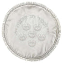 A white satin Passover Matzah cover featuring silver embroidered Hebrew text and decorative motifs, finished with a delicate lace trim.