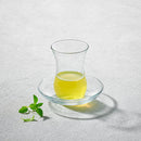 A LAV Turkish tea glass with a curved design, accompanied by a matching clear glass saucer, elegantly displayed with herbal tea.