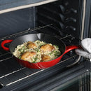 Red enameled cast iron skillet with chicken and rice baking in an oven