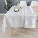 Elegant white tablecloth draped over a wooden table, featuring a decorative pattern, with a candle and glasses on a tray.
