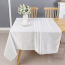 A white tablecloth drapes over a wooden table, decorated with a vase of flowers and set in a cozy dining space with two chairs.
