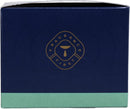 A dark blue hexagonal box with a light green bottom edge, featuring a circular gold logo in the center that reads "FRAGRANCE FIRST" around a stylized candle flame design.