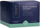 A hexagonal dark blue and light green box for a "TRAPP FRAGRANCES" candle. The box is labeled "BOB'S FLOWER SHOPPE™" with scent notes listed as "FRESH FLORALS, CUT GREEN STEMS, WATERY ACCORDS." It is a "FRAGRANCED CANDLE" weighing "3.75 oz | 106g ℮" and is identified as "No. 13".