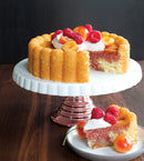 Cake with a fluted, ring-shaped design, displayed on a white cake stand on a wooden table.