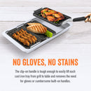 Grilling and serving set by Yukon Glory, featuring a large silver pan and three smaller black grill/sear trays with cooked food, plus a handle, all next to its product packaging.