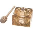 Elegant crystal honey dish with a wooden dipper and gold accents, placed on a white background.