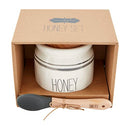 Mud Pie Bistro Honey Set in a gift box, featuring a white ceramic honey pot with black stripes and the word "HONEY," a wooden lid, and a silicone and wood honey dipper labeled "DRIZZLE."