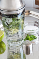 Outset 12oz glass cocktail shaker with stainless steel strainer lid, featuring printed drink recipes and measurement markings