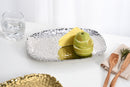 A Pampa Bay Millennium Titanium-Plated Porcelain 11-inch Platter is displayed on a white background. The silver-colored platter features a textured, hammered finish and slightly raised, irregular edges. 