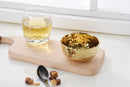 A slightly angled view of a Pampa Bay Golden Millennium Porcelain Snack Bowl. The bowl has a rich, hammered gold interior with a reflective, textured surface, and a smooth, matte off-white or cream exterior. The rim of the bowl is irregularly shaped, following the hammered texture of the interior. It is presented against a plain white background.