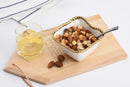 Small white porcelain snack bowl with gold titanium beaded rim filled with assorted nuts, displayed on a wooden board