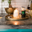 A small, cream-colored candle from Greenleaf, in the Bella Freesia fragrance, presented in a clear jar with a silver lid.