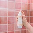 Cashmere Kiss room spray bottle with elegant floral label and pink accents on a pink tiled background.