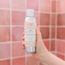 Cashmere Kiss room spray bottle with elegant floral label and pink accents on a pink tiled background.