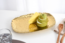 A top-down, slightly angled shot of a Pampa Bay Small Gold Serving Platter. The platter is rectangular with rounded corners and features a hammered, textured surface that gives it a dimpled appearance. Its edges are uneven and organic, and it has a shiny, reflective gold finish. The platter is positioned on a plain white or light gray background.