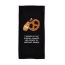 A black Mud Pie Circa Kitchen waffle weave towel featuring an embroidered illustration of a pretzel with a mustard bottle. Below the image is white embroidered text that reads: "I snack so my kitchen doesn't get lonely in between meals."